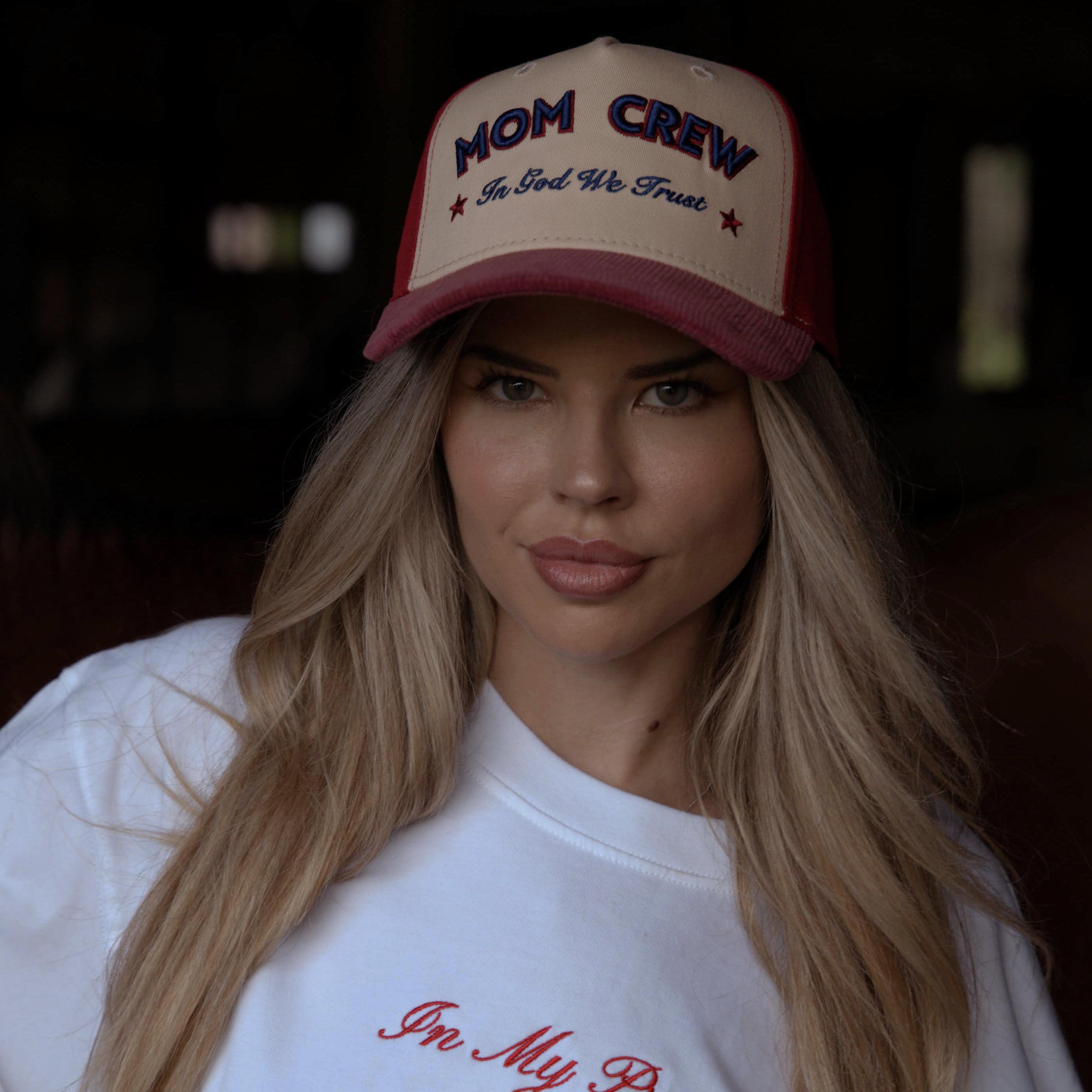 Woman wearing a white t-shirt with text and a red and white cap with text.